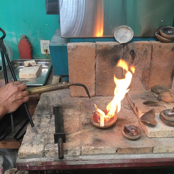A person lighting a fire in a clay bowl with a long lighter. 1