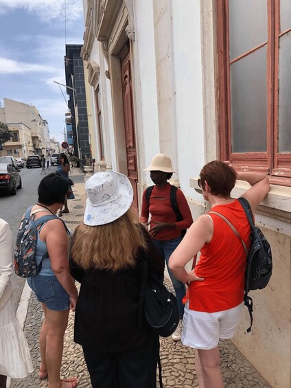 A group of people standing on a cobblestone street, looking out from a building with a red door. 5