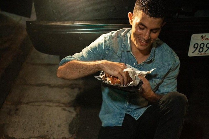 A person sitting on the ground, eating food from a tray. 2