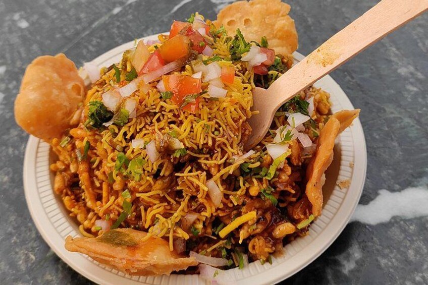 A plate of food with sev, chopped onions, tomatoes, and herbs. 3