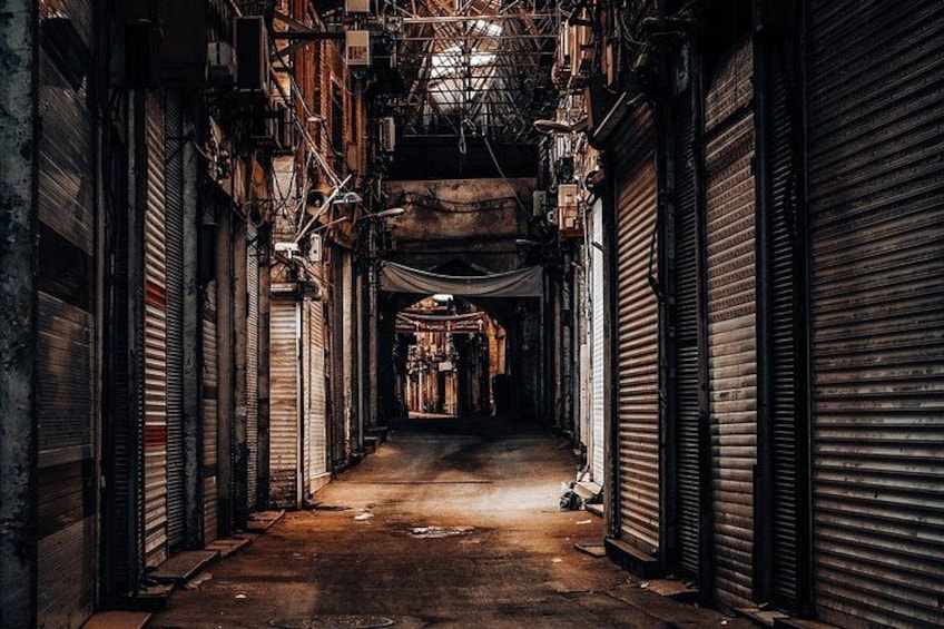 Une ruelle étroite, avec des volets métalliques fermés, des tuyaux qui la traversent et une lumière faible. 5