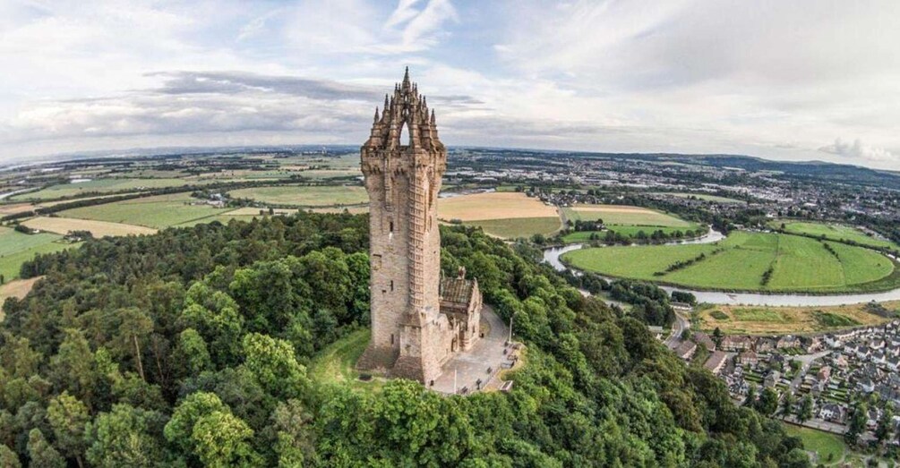 A historic tower surrounded by lush greenery and fields, with a river and town in the background. 1