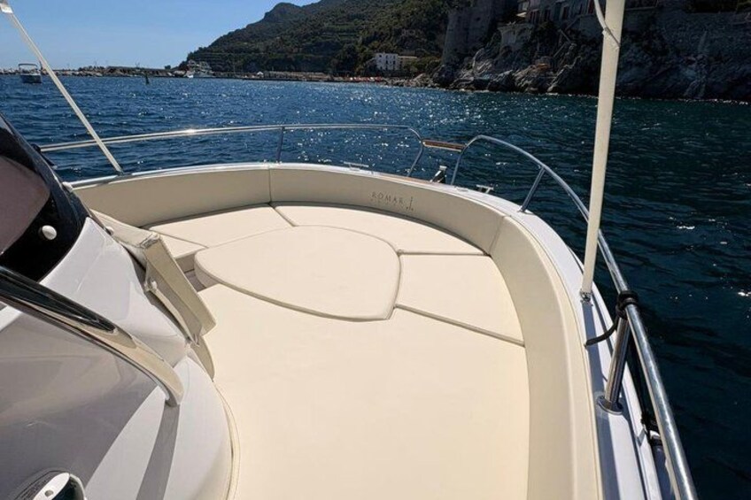 A boat's interior with a cushioned seating area, a steering wheel, and a view of the sea and rocky coastline. 4