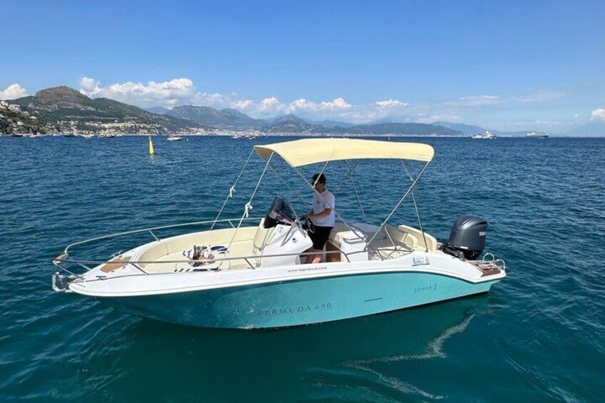 A white motorboat with a canopy on the water, a person on board, and a coastal landscape with mountains in the background. 4