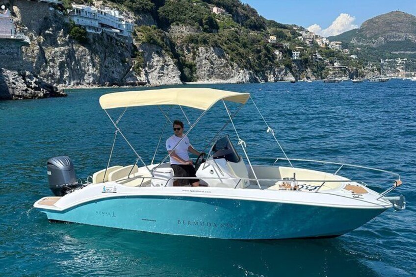 A small boat with a canopy on a calm sea, surrounded by rocky cliffs and houses. 5