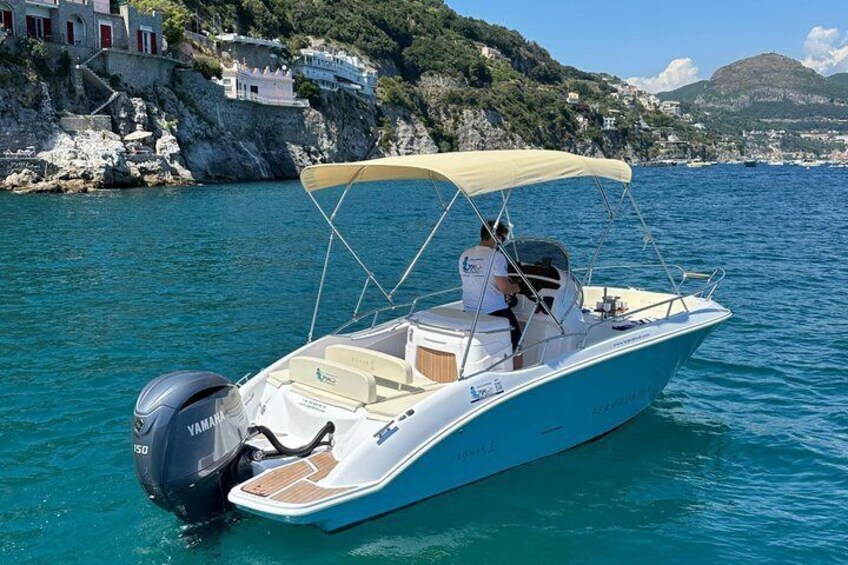 A boat with a canopy, a Yamaha outboard motor, and a cabin, docked near a coastal town with houses on a hillside. 3