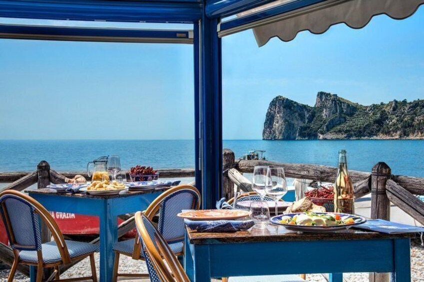 A table set with plates of food and drinks, overlooking a coastal landscape with cliffs. 1