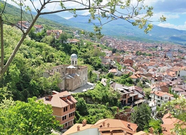 A town with a prominent church surrounded by lush greenery and a mountainous backdrop. 5