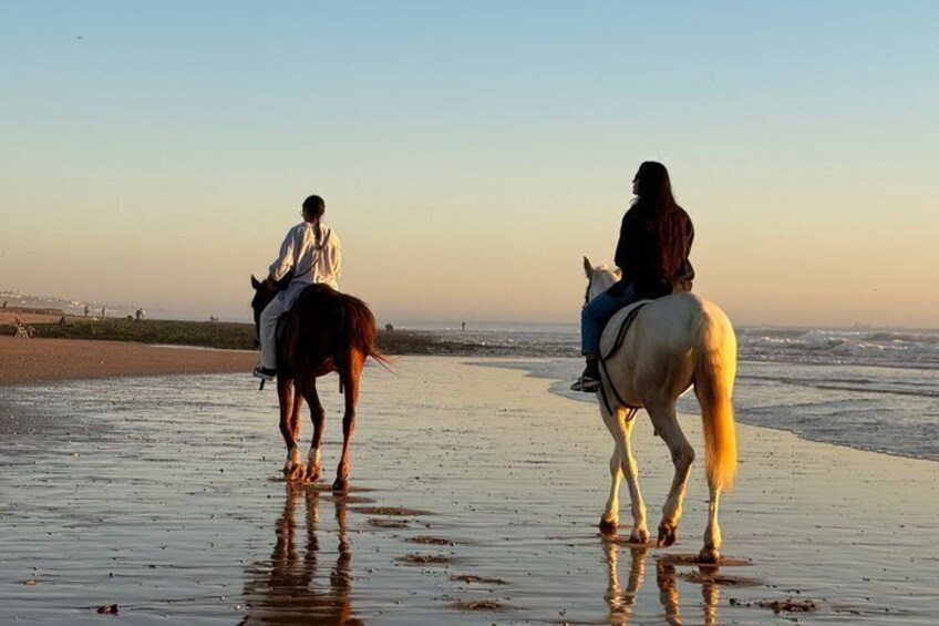 Two people riding horses along a beach with the ocean in the background. 1