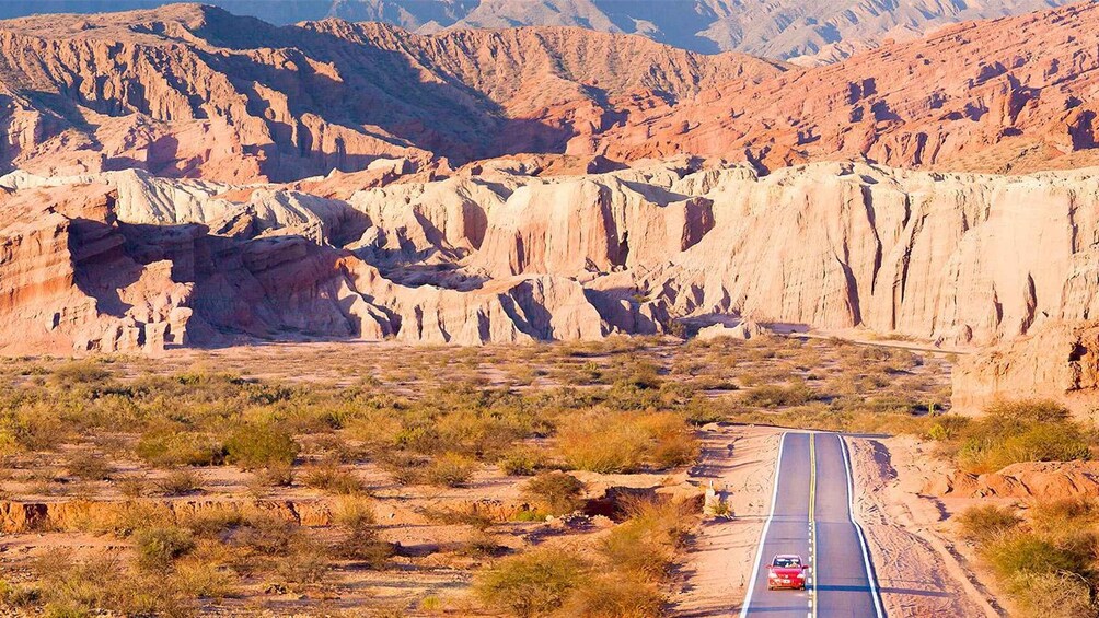 A desert landscape with a paved road and a red car driving on it. 4