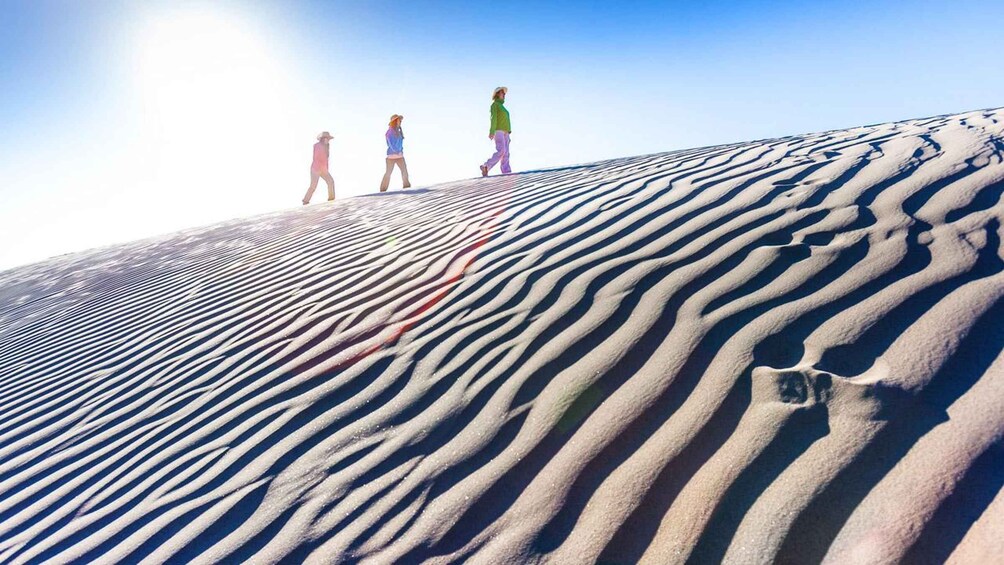 A desert landscape with rippled sand patterns and three people walking on a dune. 3