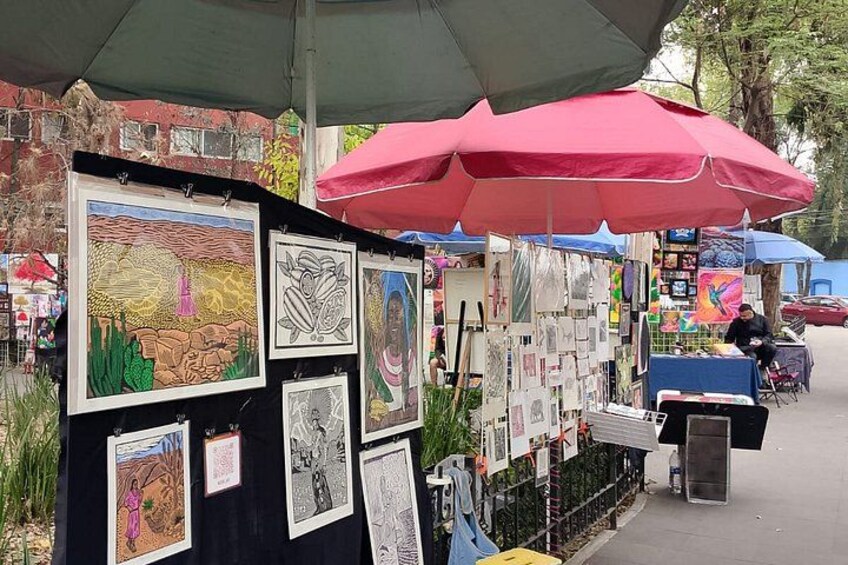 An outdoor art market with various artworks displayed under umbrellas. 3