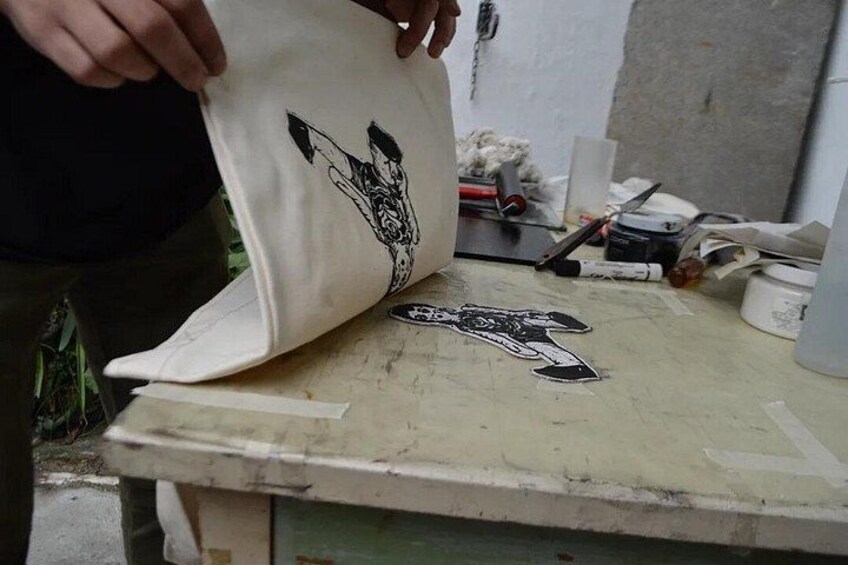 A person holding a white bag with a black design, a pair of scissors, and a cluttered workspace with various items. 2