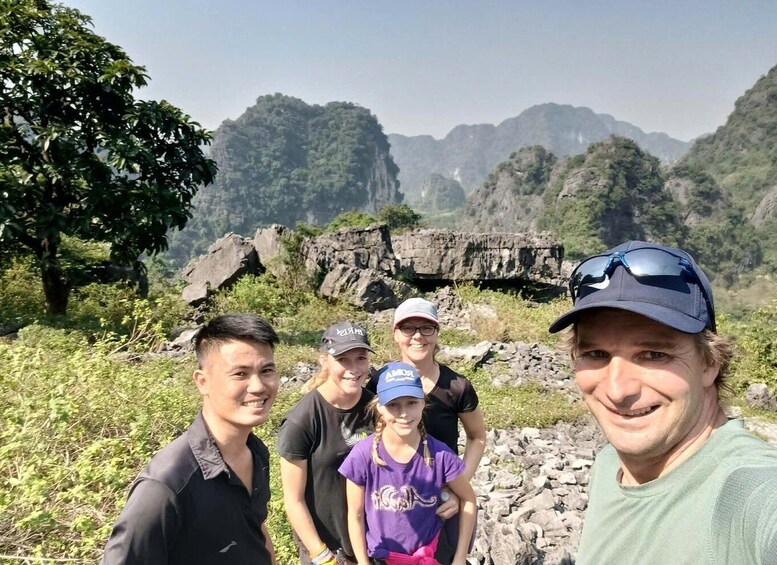 A group of people standing in a natural setting with rocky terrain and dense greenery in the background. 2