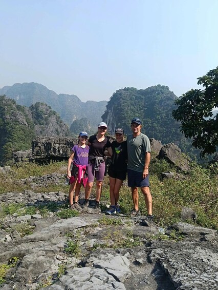 A group of people standing on rocky terrain with a mountainous landscape in the background. 3