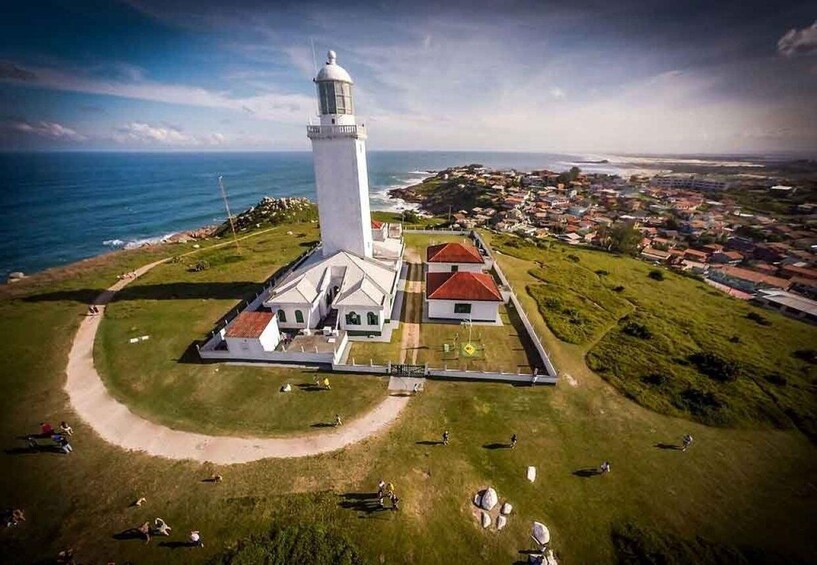 A lighthouse with a white tower, a red-roofed building, and a surrounding grassy area with a few people. 2