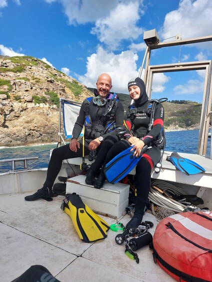 Two people in scuba diving gear sitting on a boat with diving equipment around them. 5