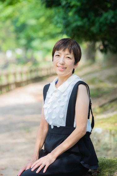 A person sitting on a stone ledge in a park with greenery in the background. 4