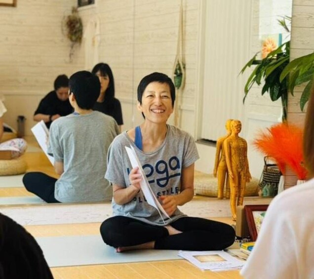 A person sitting on a mat in a room with a yoga pose, a statue, and a plant. 5