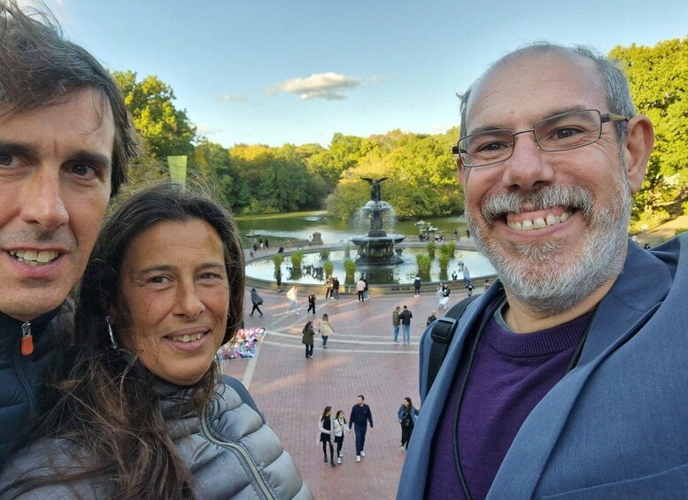 Three people standing in front of a park with a fountain and trees. 5