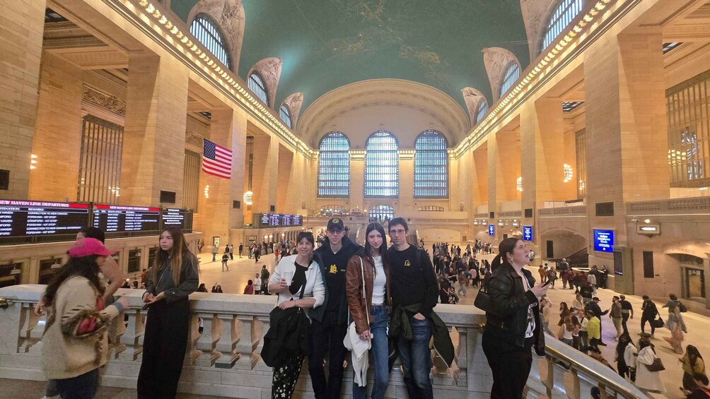 A crowded train station with large arched windows and an American flag. 3