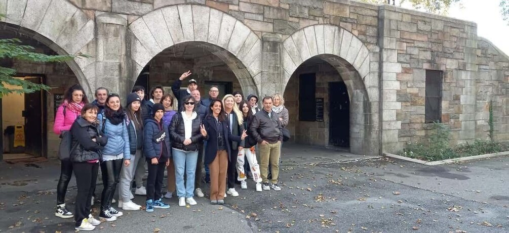 A group of people standing in front of a stone building with arched doorways. 4