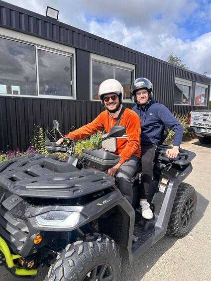 Two people on an ATV with a building in the background. 1