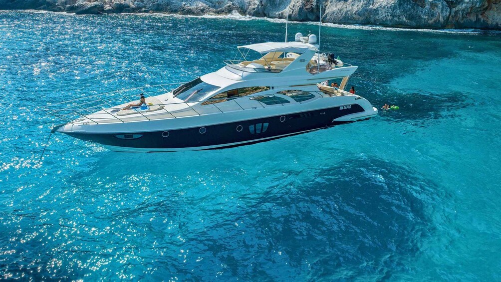 A yacht on clear blue water with rocky cliffs in the background. 1
