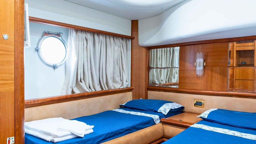 A cabin with two beds, a window with curtains, a mirror, and a small cabinet. 3