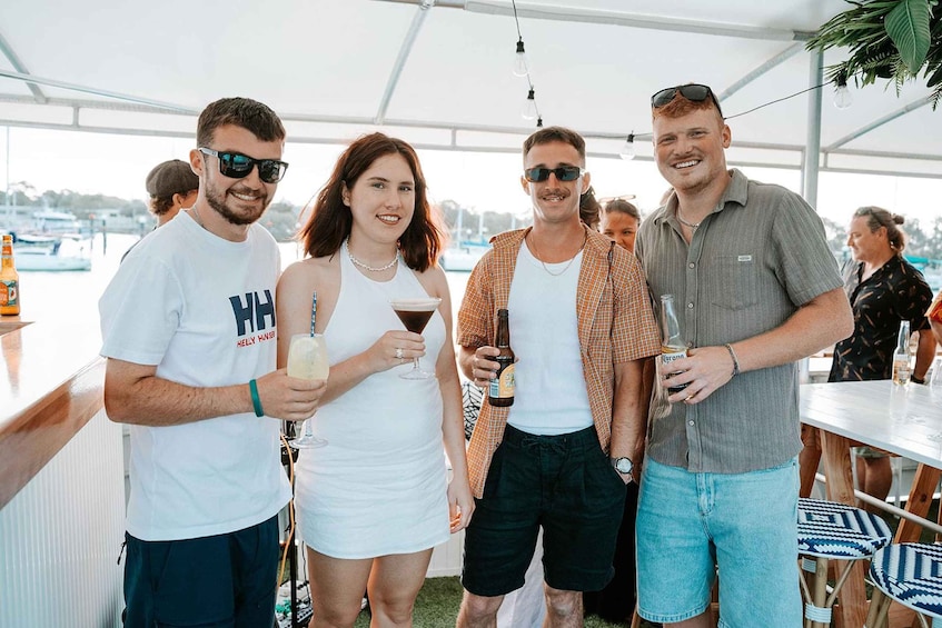 A group of people at an outdoor event with a bar and boats in the background. 5