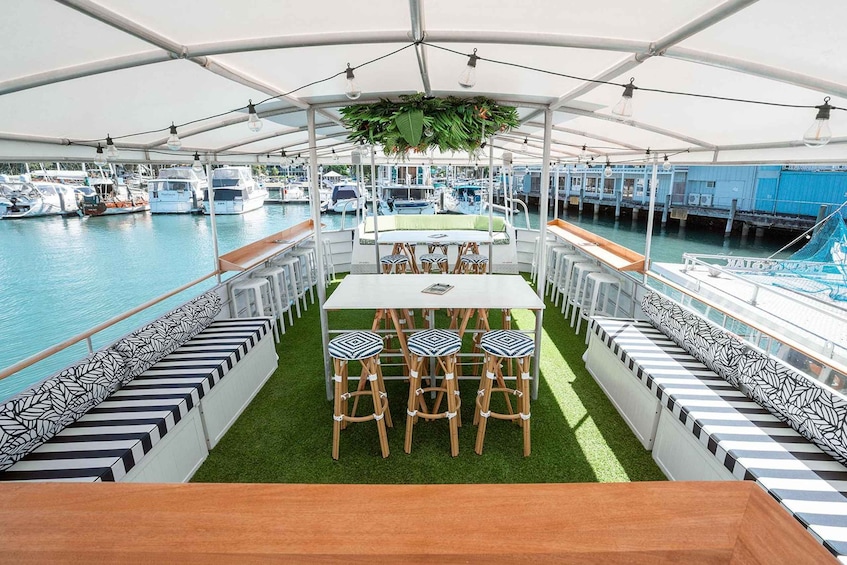A covered outdoor dining area with a table and chairs, surrounded by a railing and a view of boats in the water. 1