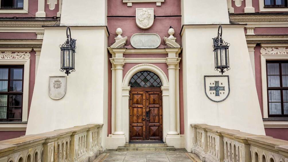 A building facade with a central arched entrance, flanked by two lanterns and a coat of arms above the door. 2