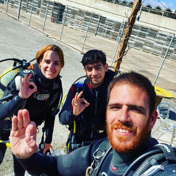 Three individuals in scuba diving gear with a metal structure and a yellow object in the background. 3