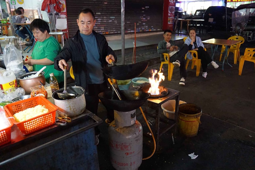 A street food vendor cooking outdoors with a gas stove and a large wok. 2