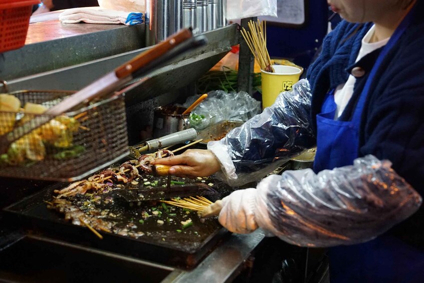 A person cooking food on a griddle, using tongs and a strainer. 3