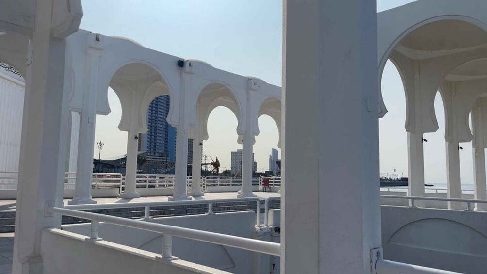 A white architectural structure with arches, a bridge, and a cityscape in the background. 3