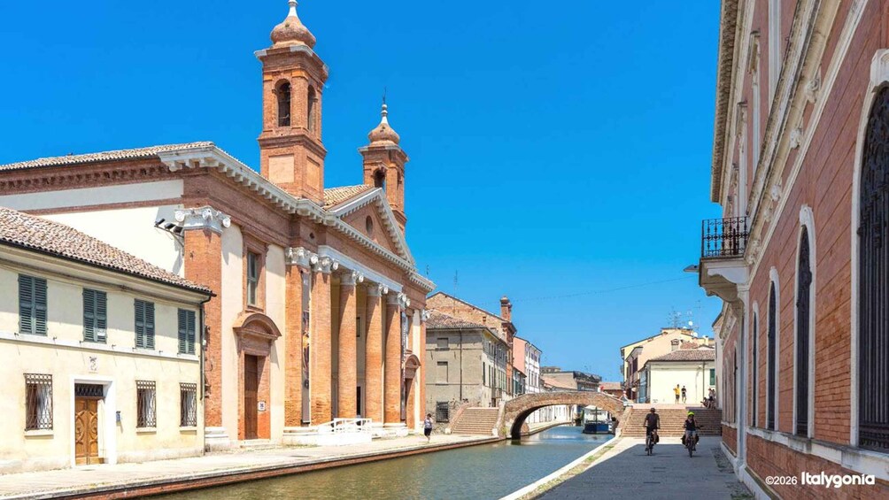 A canal with buildings on either side, a bridge, and a church with two towers. 2