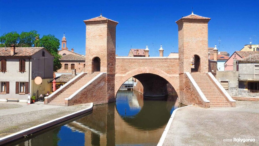 A historic stone bridge over a canal with steps leading up to it, surrounded by traditional buildings. 1