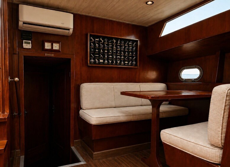 A cabin interior with a wooden wall, a framed key collection, a sofa, a table, and a porthole window. 3