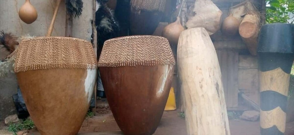 Large, brown, woven drums with a textured top, set against a rustic backdrop with a wooden structure and hanging gourds. 2