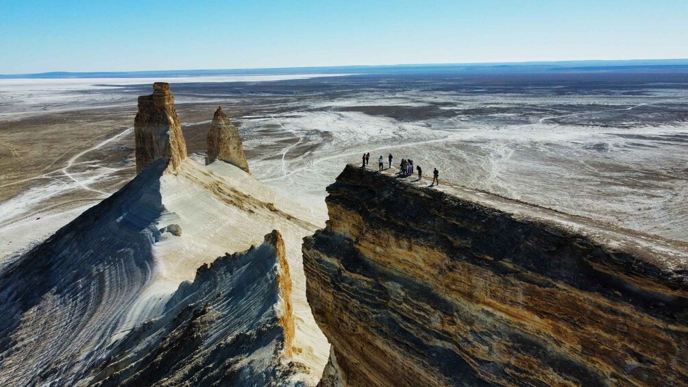 A vast salt flat with towering rock formations and a group of people standing on a cliff edge. 5