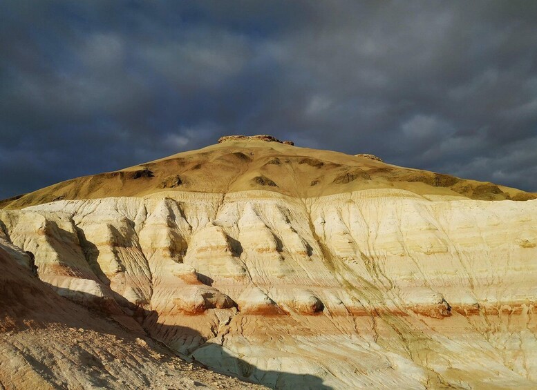 A large, layered rock formation with a flat top and steep sides, under a cloudy sky. 4