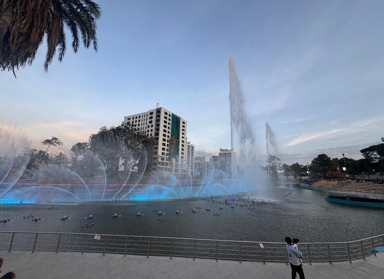 A water fountain with jets and lights, surrounded by trees and buildings. 4