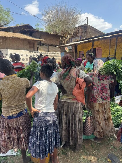 A group of people in a rural setting, some carrying leafy greens, with traditional buildings in the background. 2