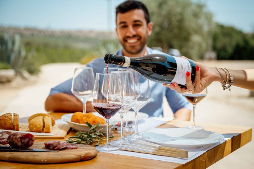 A person pouring wine into glasses at an outdoor dining table with food and a scenic background. 1