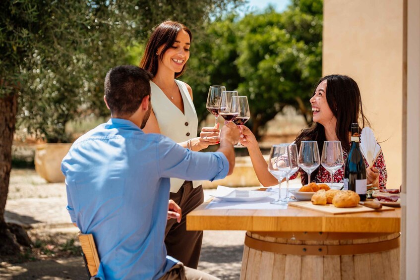 Three people toasting with wine glasses at an outdoor table with a bottle of wine and pastries. 3