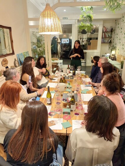 A group of people seated around a table with wine glasses and bottles, in a room with a hanging lamp and a sign that reads 'OPEN'. 2