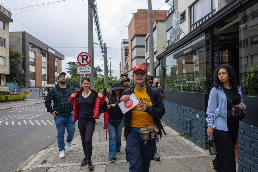 A group of people walking on a sidewalk in an urban area with buildings and a no parking sign. 1