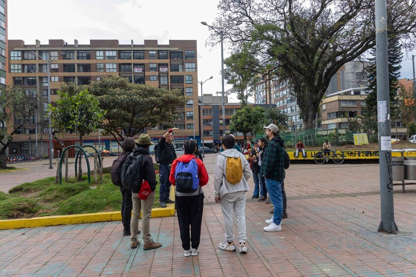 A group of people standing on a paved walkway in an urban area with buildings and trees in the background. 2