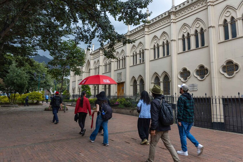A group of people walking on a brick pathway in front of a historic building with arched windows and a red umbrella. 5